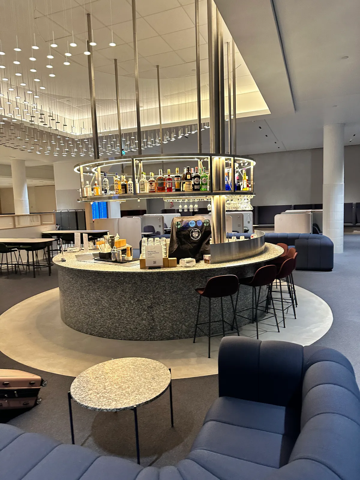 A circular granite bar stocked with bottles, ringed by stools and blue seating