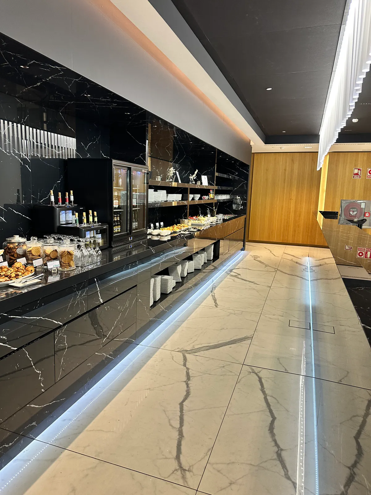 Sala VIP Joan Miro lounge buffet counter with drinks, pastries, and stacked plates