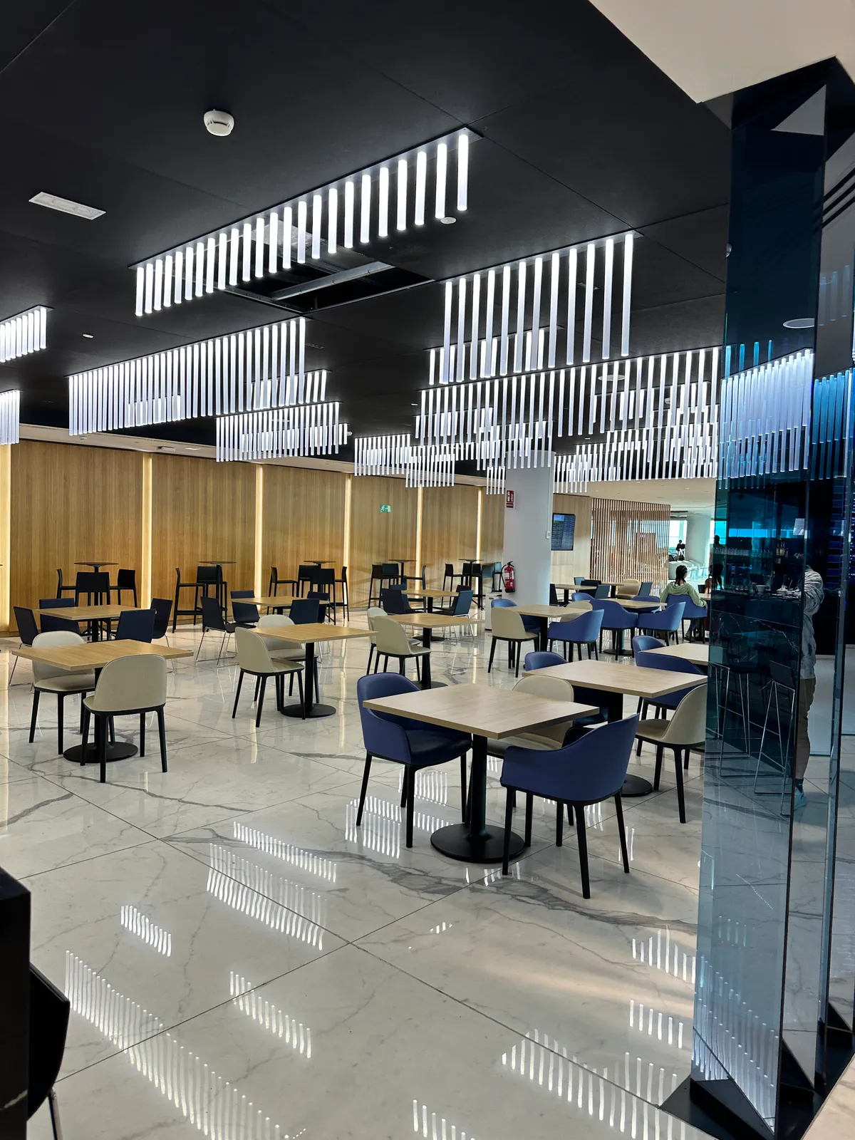 Sala VIP Joan Miro lounge dining tables under rows of hanging tube lights