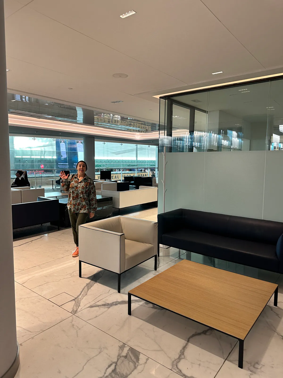 Traveler waving beside lounge sofas, a coffee table, and the terminal windows