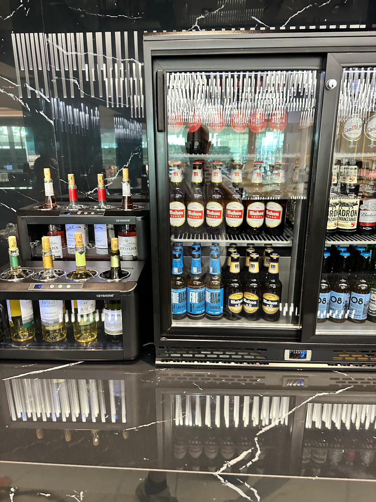 Lounge wine dispensers beside a glass-door fridge stocked with beer