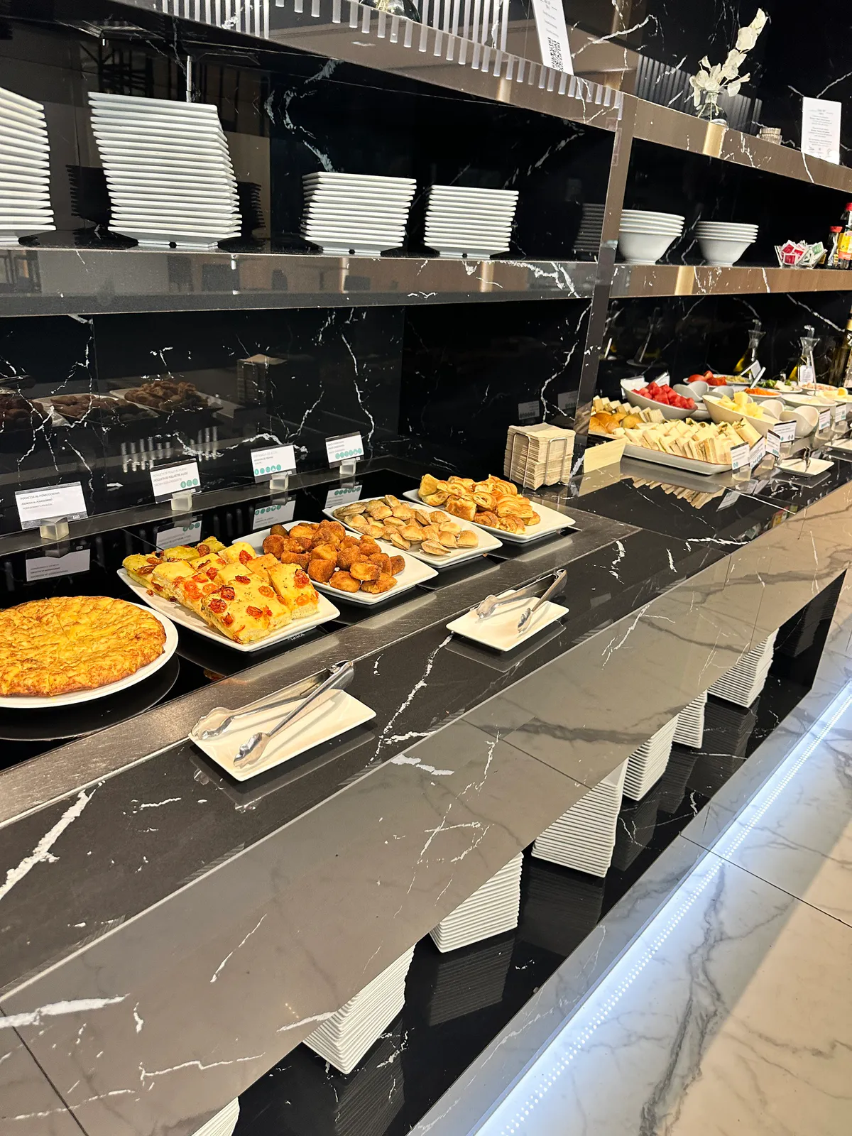 Lounge hot buffet with tortilla, focaccia, fried snacks, and stacked white plates