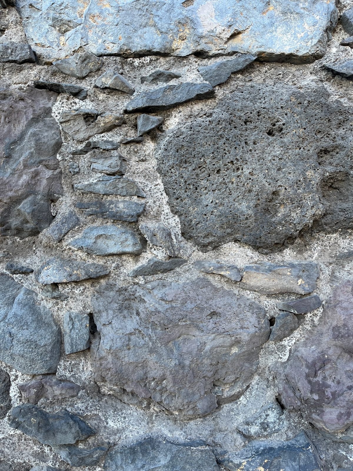 Close-up of a rough wall built from gray stones and porous volcanic rock.