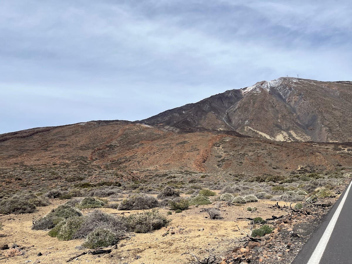 Snow-dusted Teide rising above dry scrubland beside a paved road