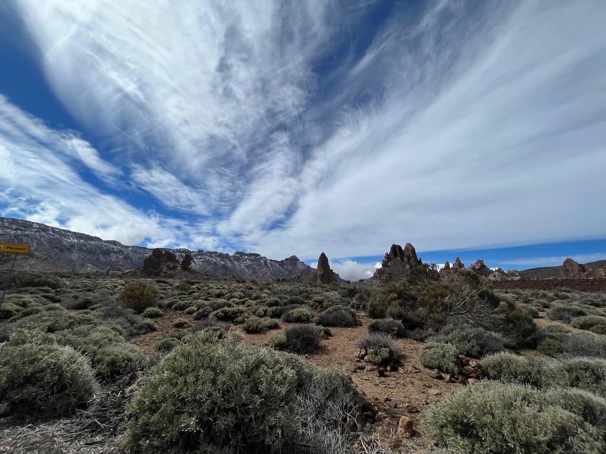 Jagged rock spires beyond gray shrubs, with a yellow Parador sign at left