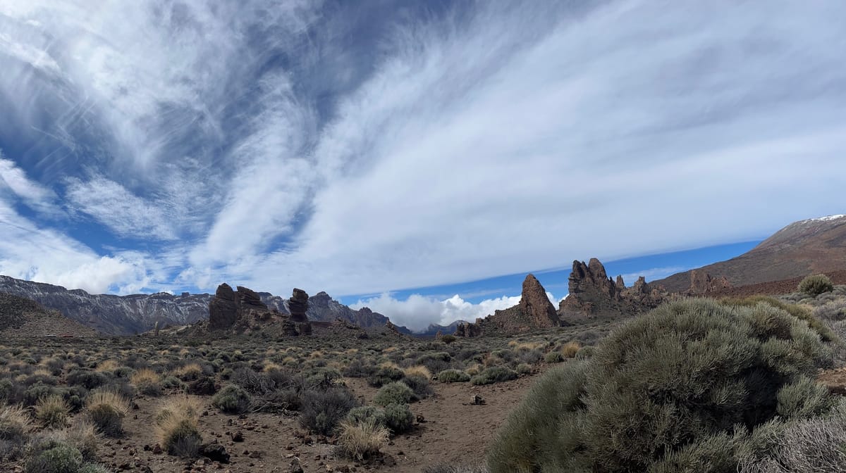 Wide view of rock spires and snow-streaked ridges across a shrub plain