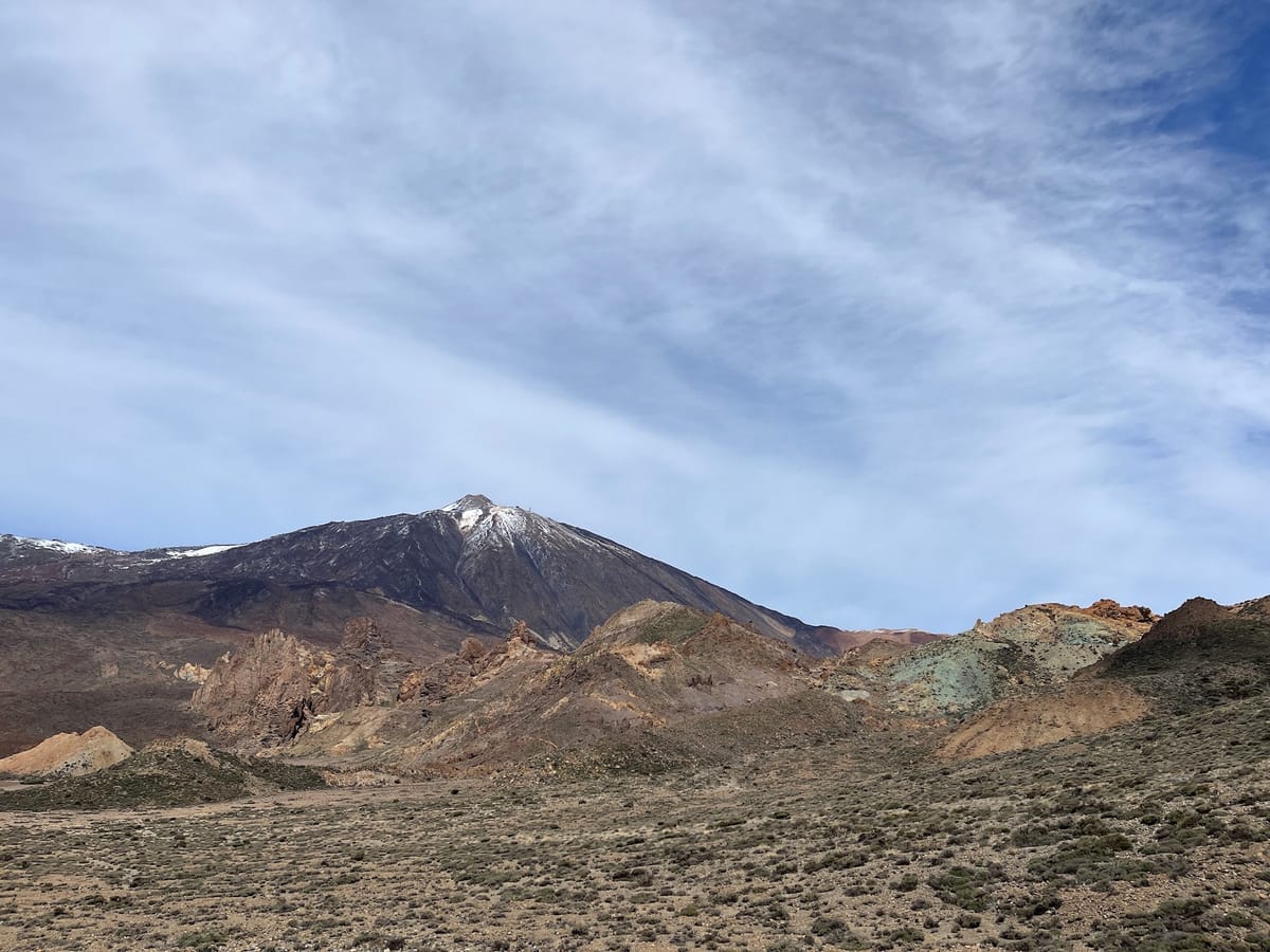 Snow-capped Teide rising behind rust, ochre, and green volcanic hills