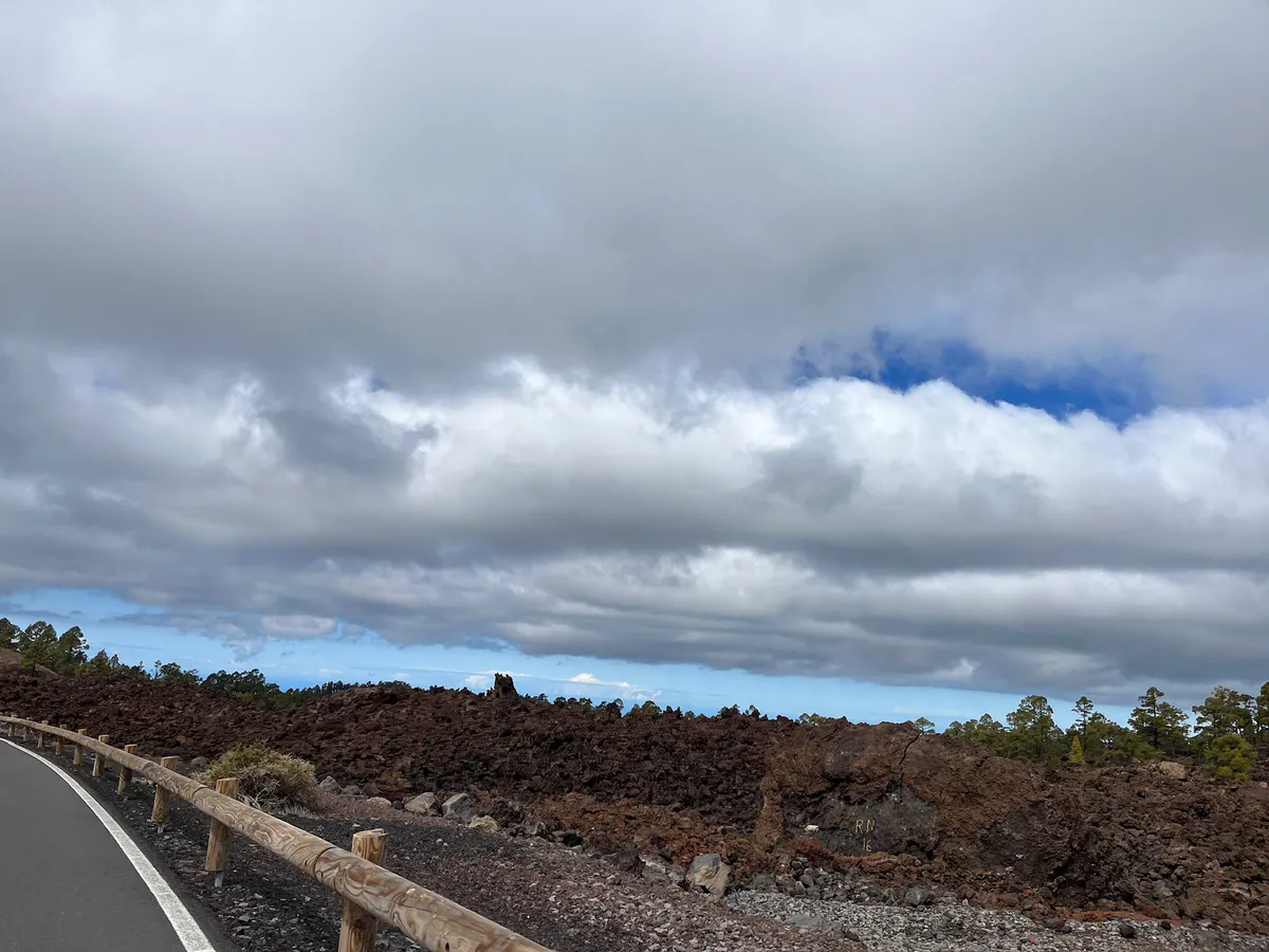 Wooden guardrail along a road beside a dark lava field under heavy clouds