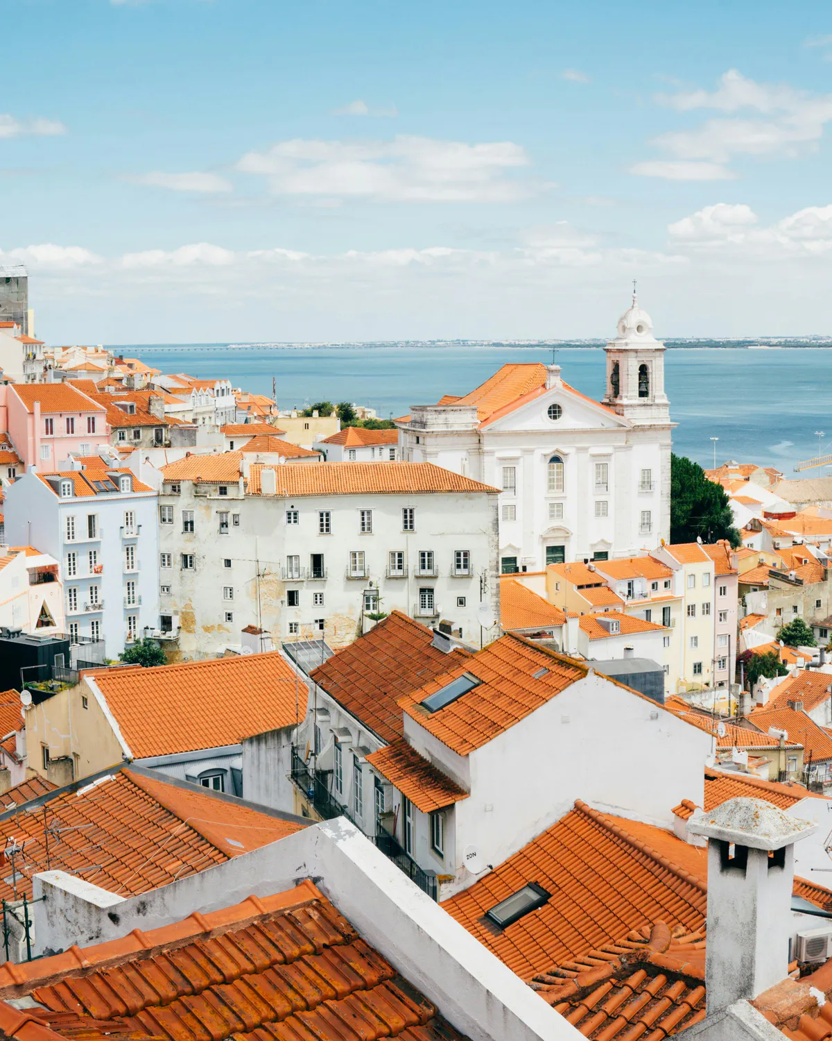 Lisbon rooftops with orange tiles, a white church, and the sea