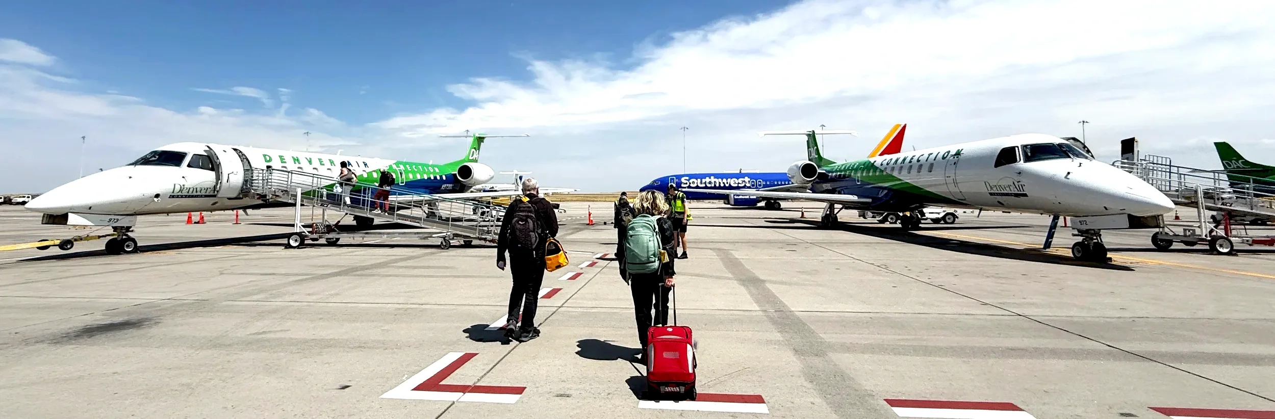 Travelers with luggage walking toward Denver Air Connection and Southwest jets