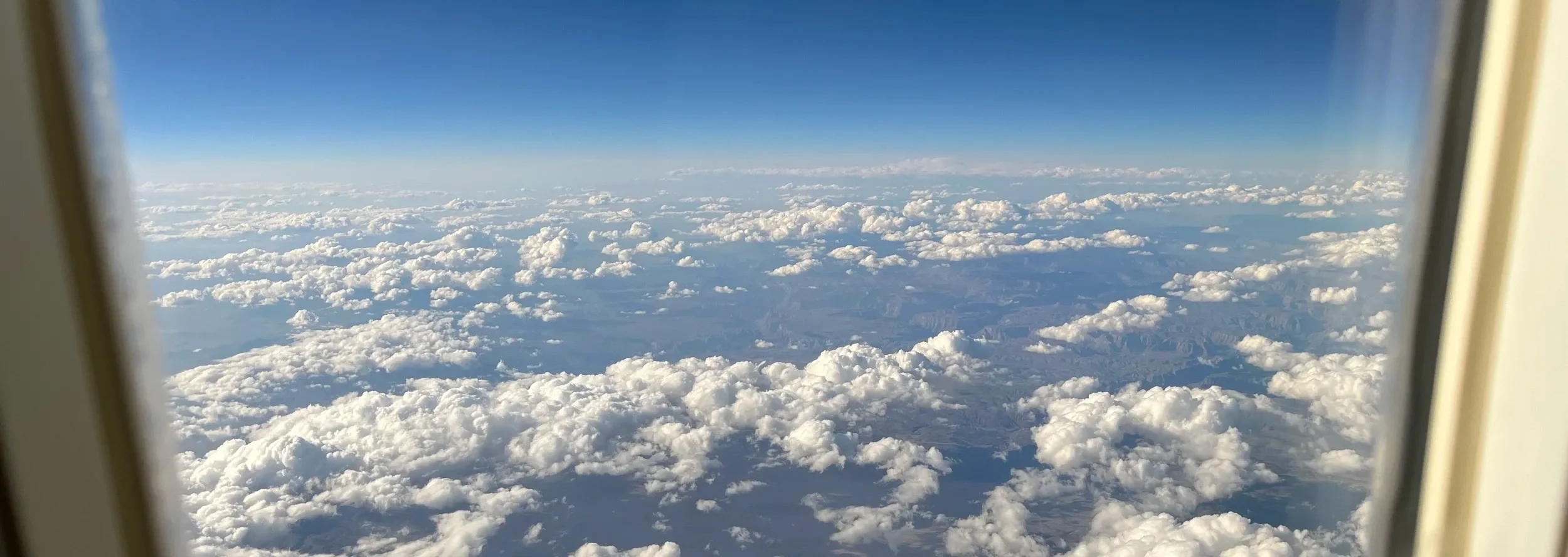 Airplane window view of clouds over distant mountains